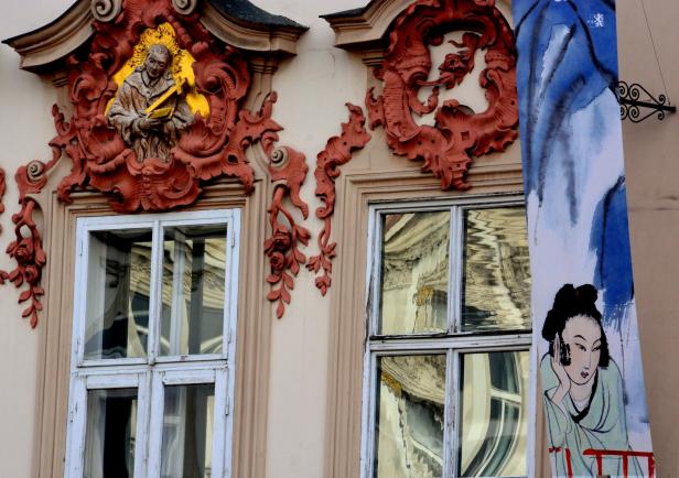 Detail einer Fassade mit Fenster, Skulptur und einem Banner mit einer asiatischen Frau.