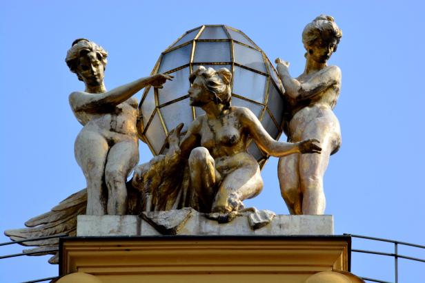 Eine goldene Skulptur von drei weiblichen Figuren und einer Weltkugel auf einem Gebäude.
