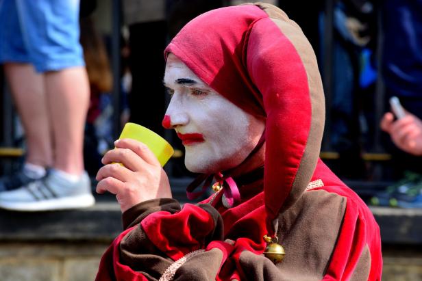 Ein Mann in einem Narrenkostüm trinkt aus einem gelben Becher.