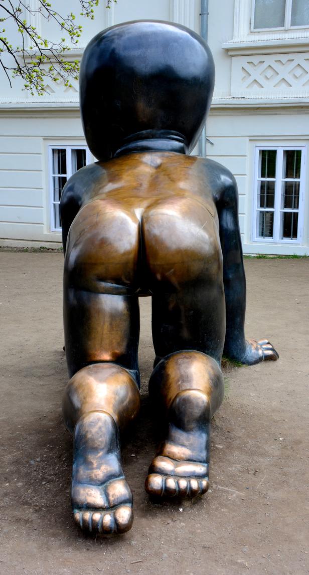 Die Rückseite einer kriechenden Baby-Skulptur vor einem Gebäude.