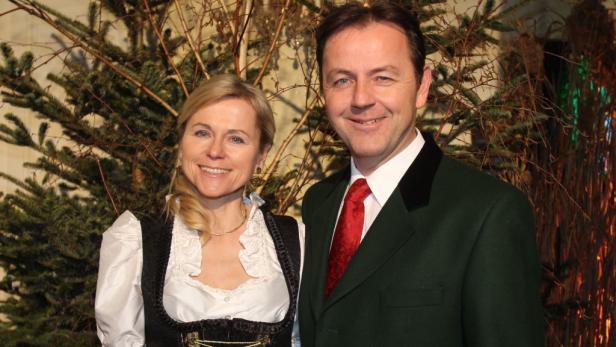 Ein Mann im Trachtenanzug und eine Frau im Dirndl posieren vor einem dekorierten Hintergrund.