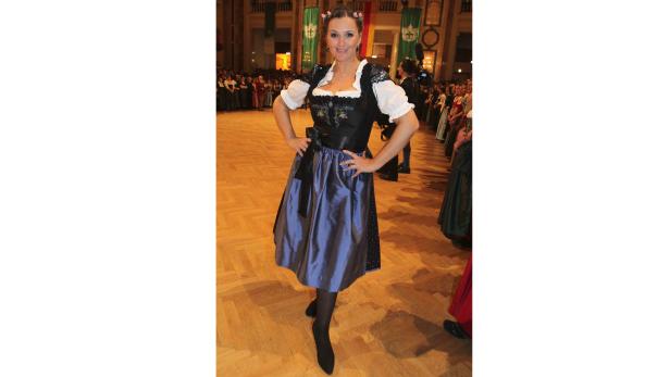 Eine Frau im Dirndl posiert auf einem Ballsaal-Parkettboden.