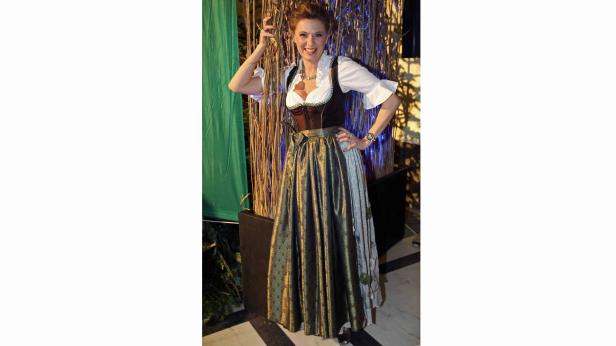 Eine Frau in einem Dirndl posiert lächelnd vor einem dekorierten Hintergrund.