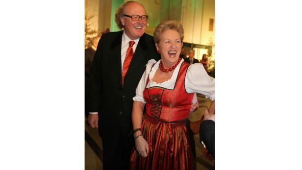 Ein Mann im Anzug und eine Frau im Dirndl lachen zusammen.