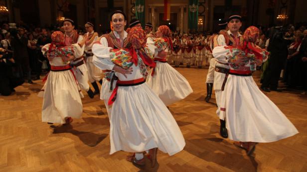 Eine Gruppe von Paaren tanzt in traditionellen Trachten auf einem Parkettboden.