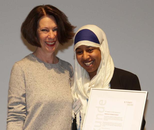 Zwei Frauen, eine davon mit Kopftuch, lächeln mit einer Urkunde in die Kamera.