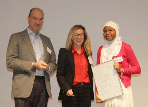 Eine junge Frau mit Kopftuch erhält eine Urkunde von zwei Personen.