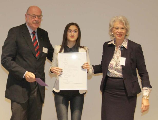 Eine junge Frau wird von zwei älteren Personen für ihre Urkunde geehrt.