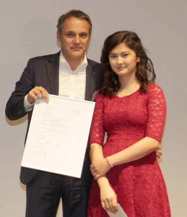 Ein Mann im Anzug überreicht einer jungen Frau in einem roten Kleid eine Urkunde.