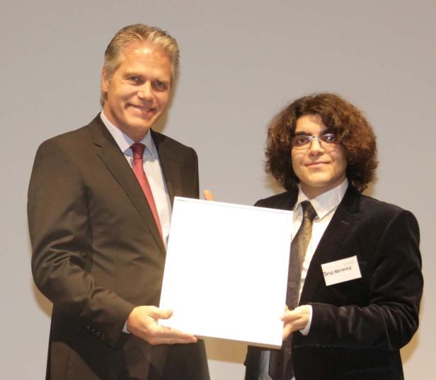 Ein Mann im Anzug überreicht Parsa Karimika eine Auszeichnung.