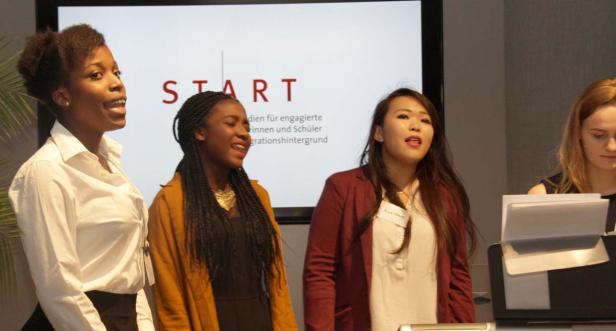 Eine Gruppe junger Frauen singt vor einer Leinwand mit der Aufschrift „START“.