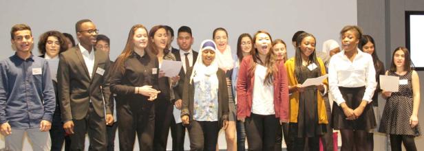 Eine vielfältige Gruppe junger Menschen steht auf einer Bühne und singt.