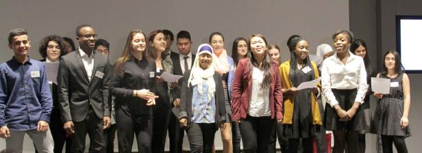 Eine Gruppe junger Leute steht auf einer Bühne und hält Papiere in den Händen.