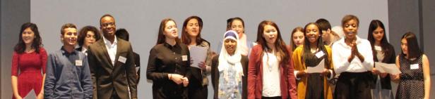 Eine vielfältige Gruppe junger Menschen steht auf einer Bühne und singt.