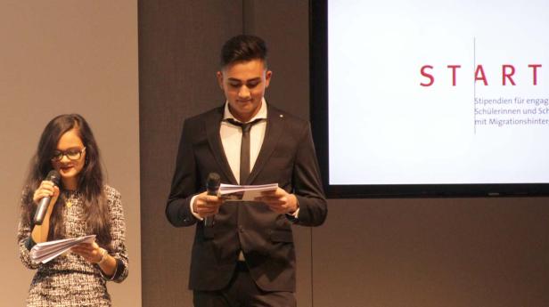 Eine Frau und ein Mann halten Reden vor einer Leinwand mit der Aufschrift „START Stipendien“.