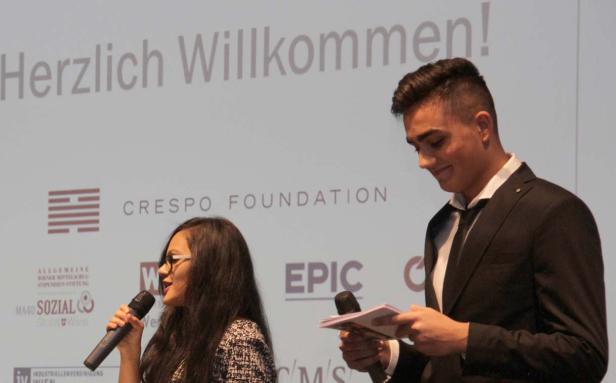 Eine Frau und ein Mann präsentieren auf einer Bühne mit dem Schriftzug „Herzlich Willkommen!“.