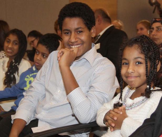 Eine Gruppe lächelnder Kinder sitzt zusammen bei einer Veranstaltung.