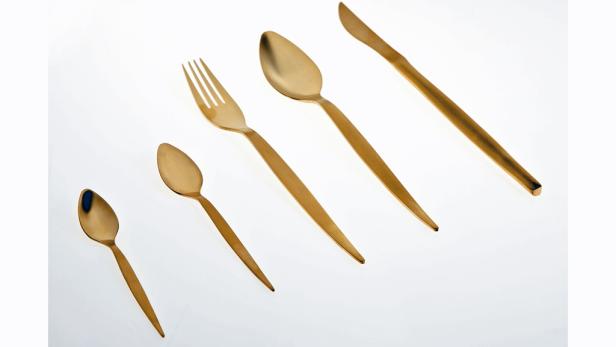 Fünf goldene Besteckteile liegen auf einem weißen Hintergrund.