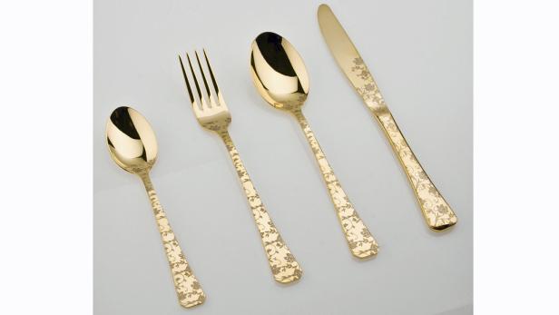 Ein Set aus goldfarbenem Besteck mit floralen Mustern liegt auf einem Tisch.