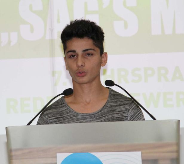 Ein junger Mann spricht an einem Rednerpult vor einem Publikum.