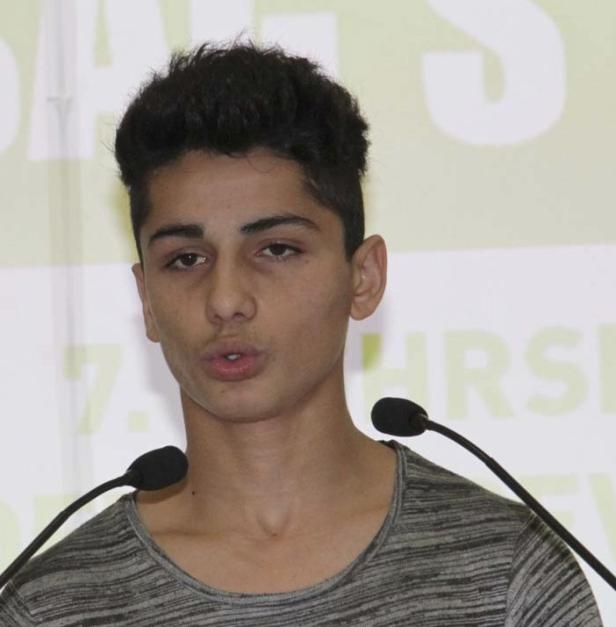 Ein junger Mann spricht an einem Rednerpult mit zwei Mikrofonen.