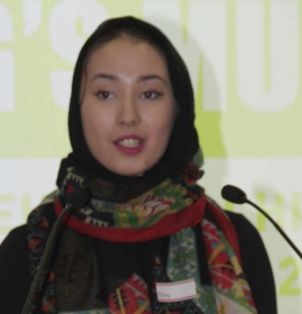 Eine junge Frau mit Kopftuch spricht bei einer Veranstaltung in ein Mikrofon.