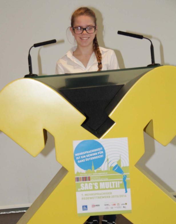 Eine junge Frau steht an einem gelben Rednerpult mit Mikrofonen.