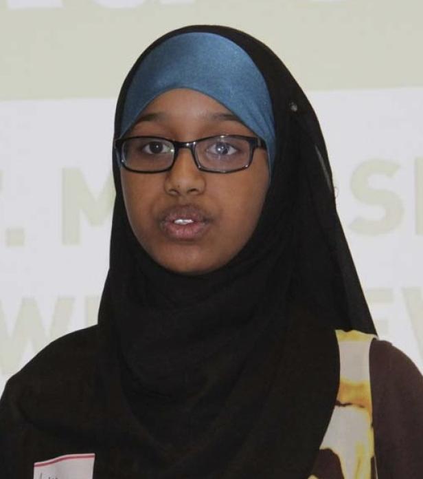 Eine junge Frau mit Brille und Hijab spricht vor einem Publikum.