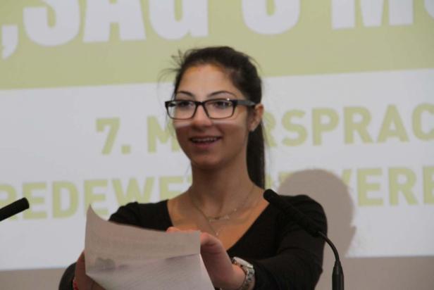 Eine junge Frau hält ein Blatt Papier vor einem Mikrofon und lächelt.