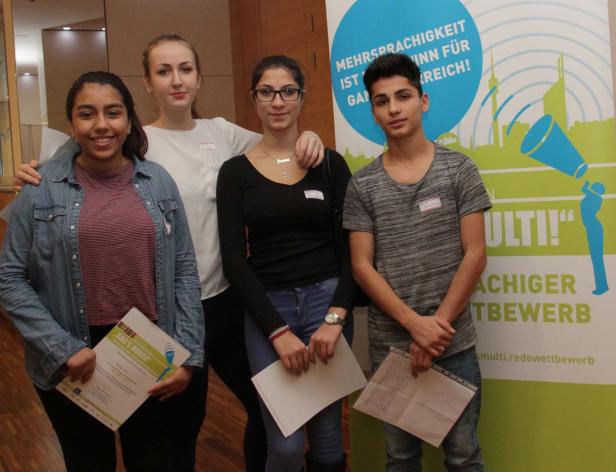Vier Jugendliche stehen vor einem Banner des Wettbewerbs „Sag’s Multi!“.