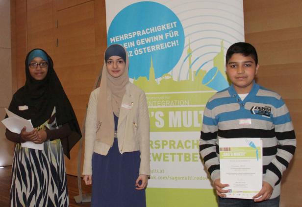Drei Jugendliche stehen vor einem Banner für den Wettbewerb „Sag’s Multi“.