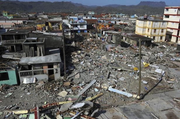 Ein zerstörtes Wohngebiet mit Trümmern und beschädigten Häusern nach einer Katastrophe.