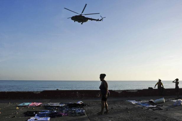 Ein Hubschrauber überfliegt eine Küstenlinie, wo Menschen Wäsche zum Trocknen auslegen.