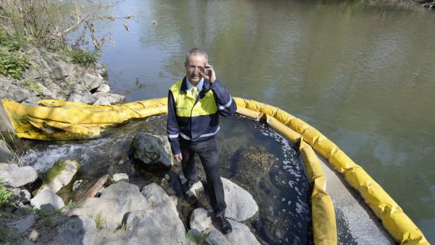 Ein Mann in Arbeitskleidung steht an einem Fluss mit einer gelben Ölsperre.