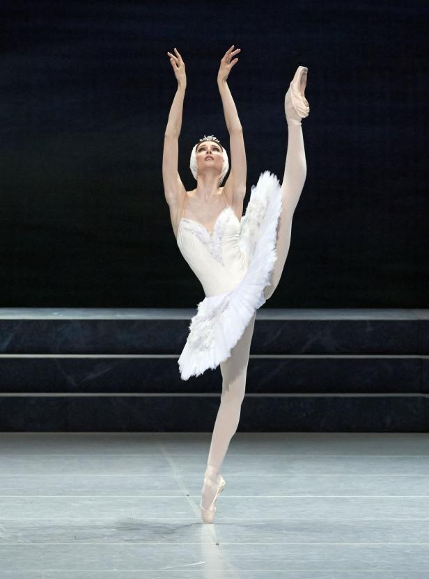 Eine Ballerina in einem weißen Tutu führt eine Arabesque auf der Bühne auf.