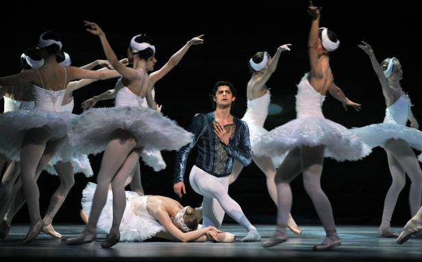 Ein Ballett-Ensemble führt „Schwanensee“ auf einer dunklen Bühne auf.