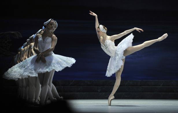 Eine Ballerina tanzt anmutig auf der Bühne, während andere Tänzerinnen im Hintergrund zu sehen sind.