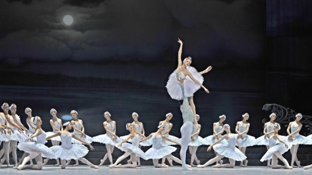Eine Aufführung von „Schwanensee“ mit Ballerinen in weißen Tutus vor einem Bühnenbild mit Mond.