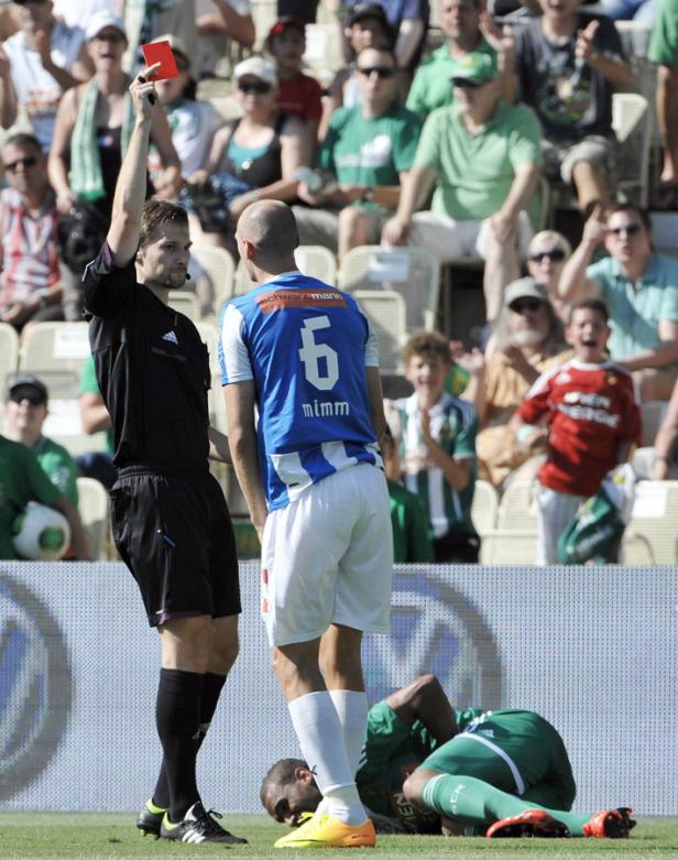 Ein Schiedsrichter zeigt einem Fußballspieler die Rote Karte, während ein anderer am Boden liegt.