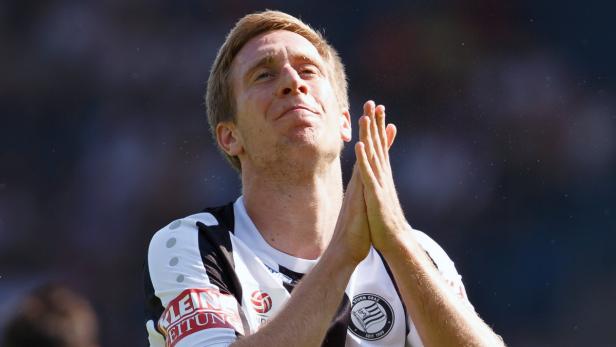 Ein Fußballspieler von Sturm Graz klatscht mit einem Lächeln im Gesicht.