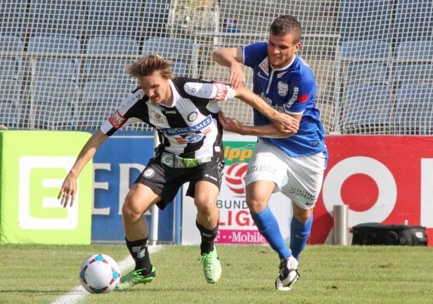 Zwei Fußballspieler kämpfen um den Ball auf dem Spielfeld.
