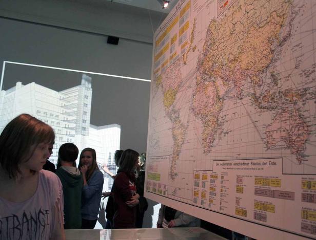 Eine Gruppe von Menschen betrachtet eine große Weltkarte in einer Ausstellung.