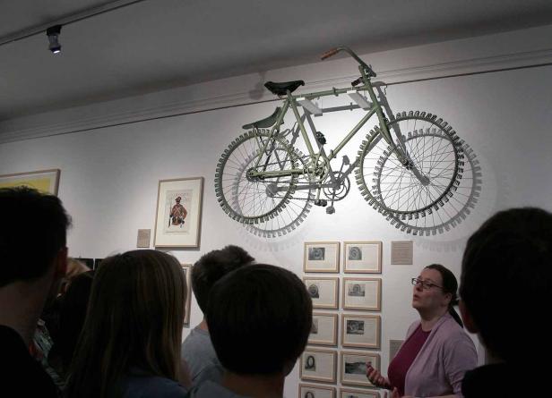 Besucher betrachten ein Fahrradkunstwerk mit ungewöhnlichen Reifen in einer Galerie.