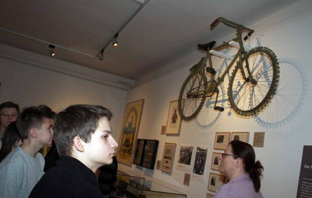 Besucher betrachten ein an der Wand montiertes Fahrrad in einem Museum.