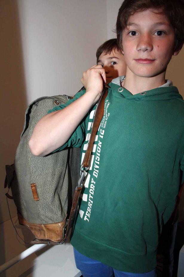 Ein Junge mit einem alten Armeerucksack und einem grünen Kapuzenpullover.