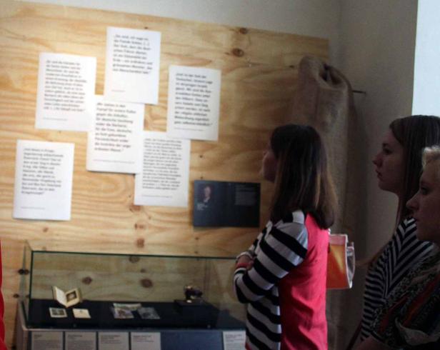 Besucherinnen betrachten eine Ausstellung mit Texttafeln und Objekten in Vitrinen.