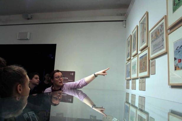 Eine Frau erklärt einer Gruppe von Menschen die Bilder in einer Kunstausstellung.