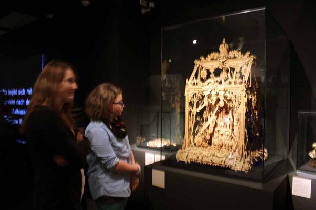 Zwei Besucherinnen betrachten eine aufwändige, geschnitzte Krippe in einem Museum.