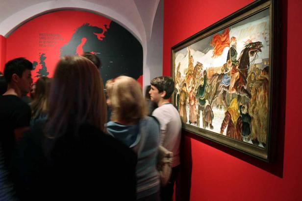 Besucher betrachten ein Gemälde in einem Museum mit roter Wandfarbe.