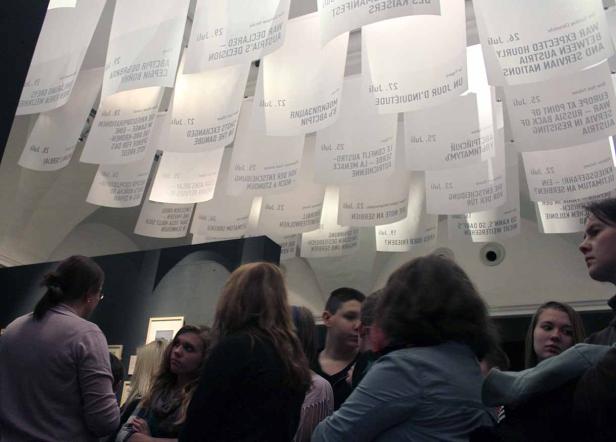 Menschen betrachten eine Kunstinstallation mit von der Decke hängenden Papierbögen.